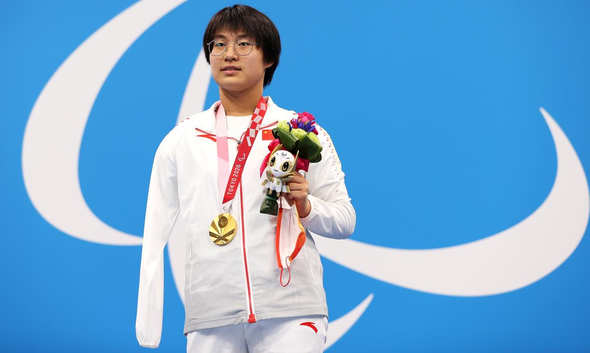 A woman poses with a gold medal, holding the mascot in her left hand