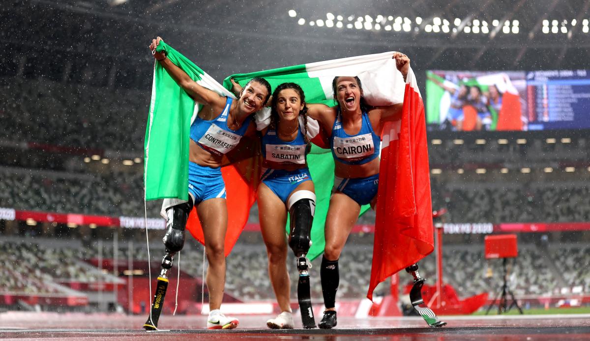 Three female athletes posing for a photo with flags while the rain is falling