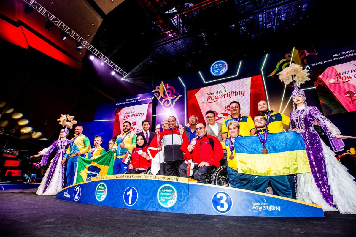 Athletes on the podium with team representatives posing for a photo with flags.