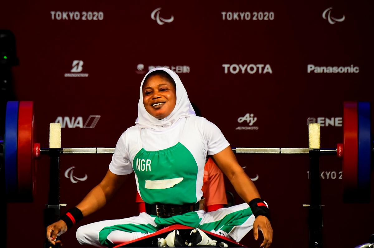 A woman sitting on the bench with her legs crossed and a smile on her face.