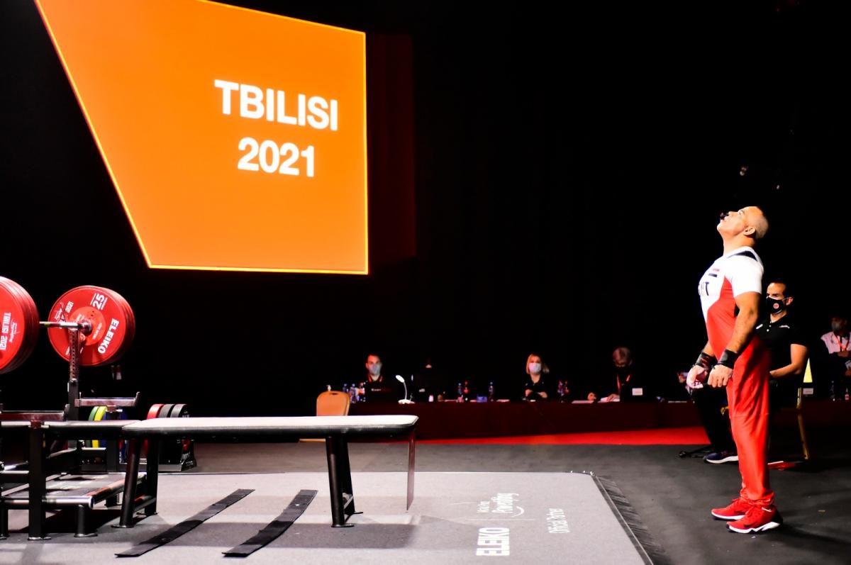 A man standing in front of a bench press in a Para powerlifting competition