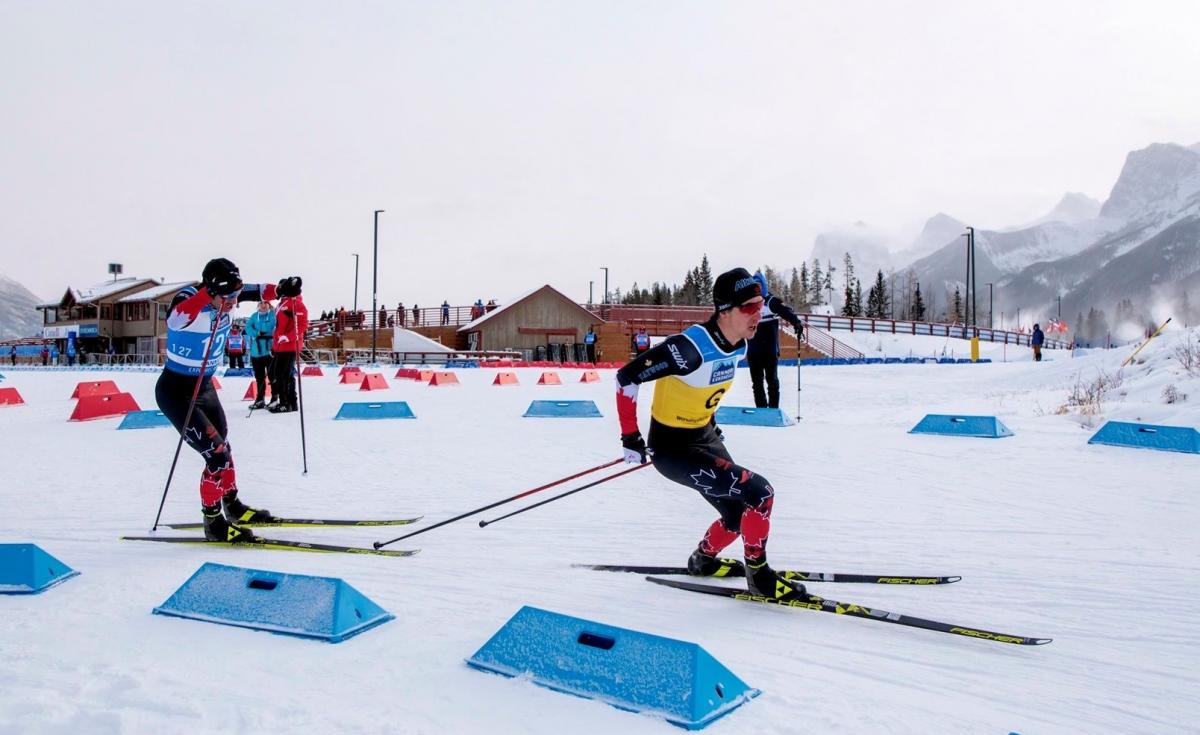 A male cross-country skier following his guide on a snowy track observed by three people