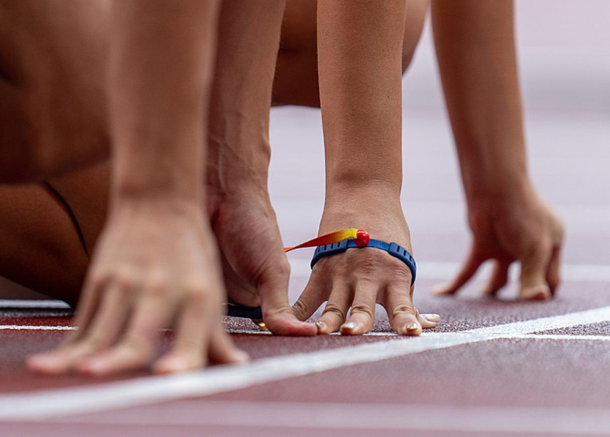 Two pairs of hands side by side on an athletics track starting line