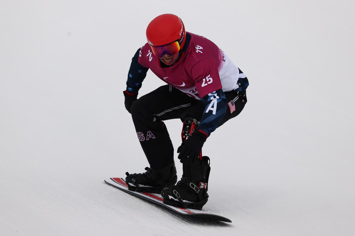 A man on a snowboard going down the snow with a helmet and goggles on his head.