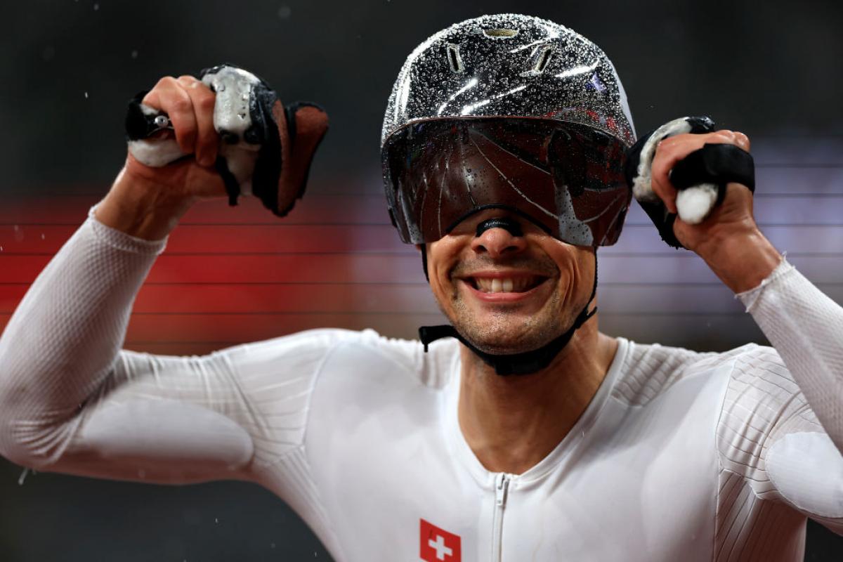 Switzerland's Marcel Hug wears a silver helmet that is shining with rain droplets and raises his hands to celebrate his victory in the men’s 800m T54 final