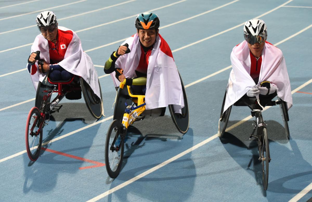 Three men in racing wheelchairs on an athletics track