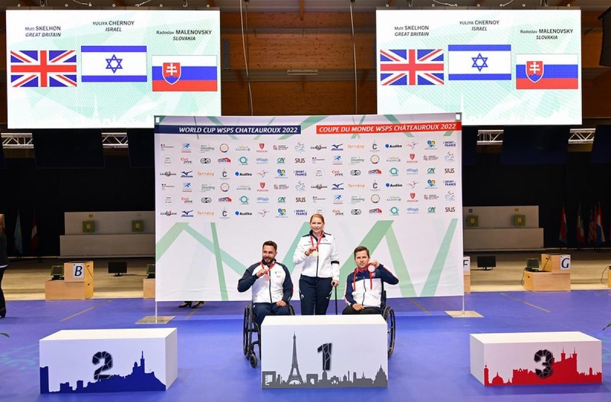 A woman standing on a podium between two men in wheelchairs