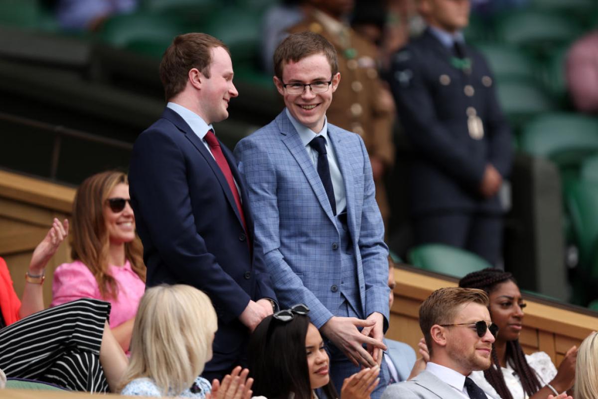 Two young men stand and smile as people around them sit and clap.