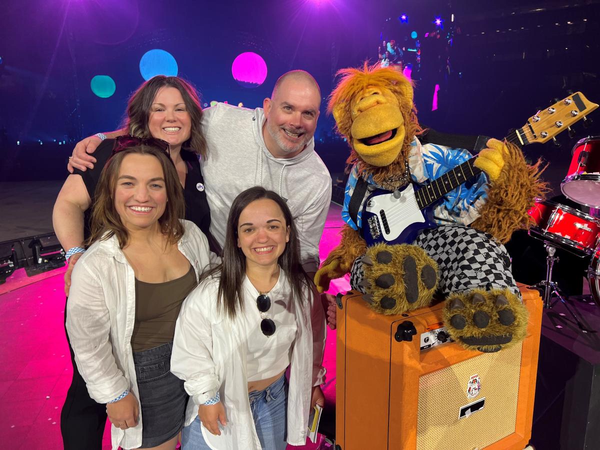 Two swimmers, a coach and manager pose with a puppet from the fictional band The Weirdos.