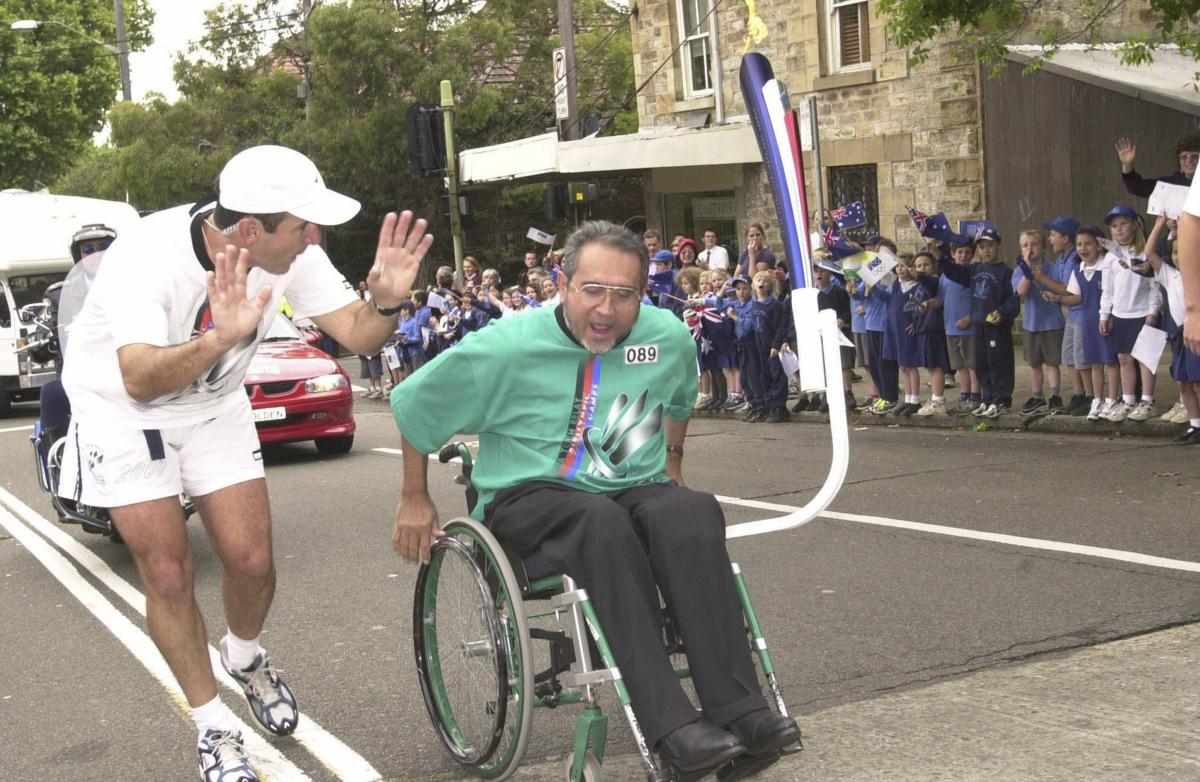 A man pushes his wheelchair in front of a crowd of young spectators as part of the Sydney 2000 torch relay.