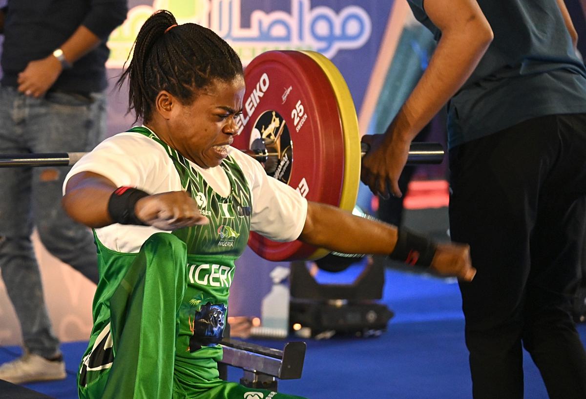 A woman in a green jersey and a white T-Shirt raises her arms and makes a strong gesture with her face.