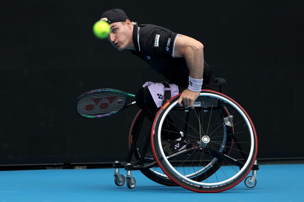 A male wheelchair tennis player eyes the ball with focus as he prepares to return it during a match.