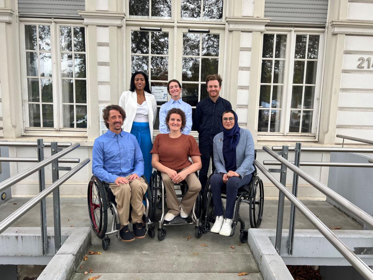 a group of male and female Para athletes sitting and standing outside a white building