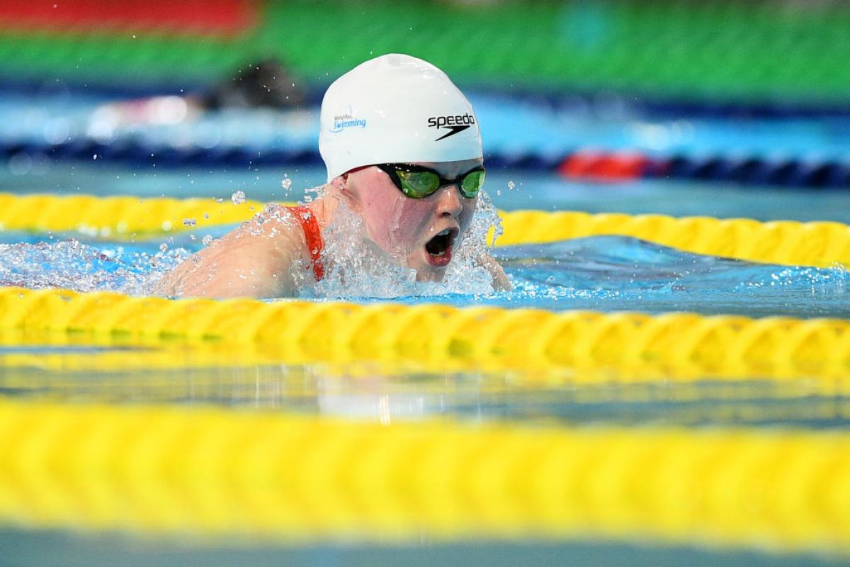 A female swimmer with a white cap swimming backstroke