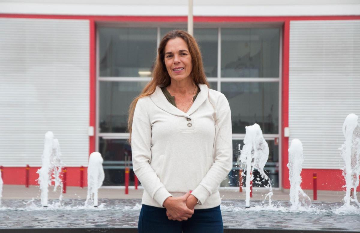 A woman poses for a photo in front of a fountain with her hands clasped together.