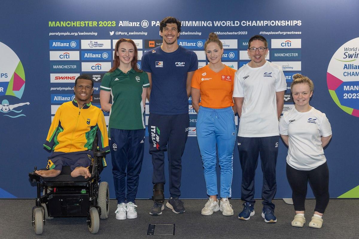 A male wheelchair posing for a picture next to a woman and a group of two men and other two women