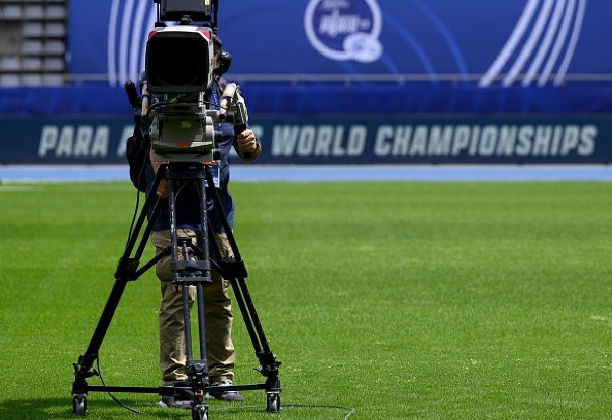 A TV camera on a grass pitch in an athletics stadium