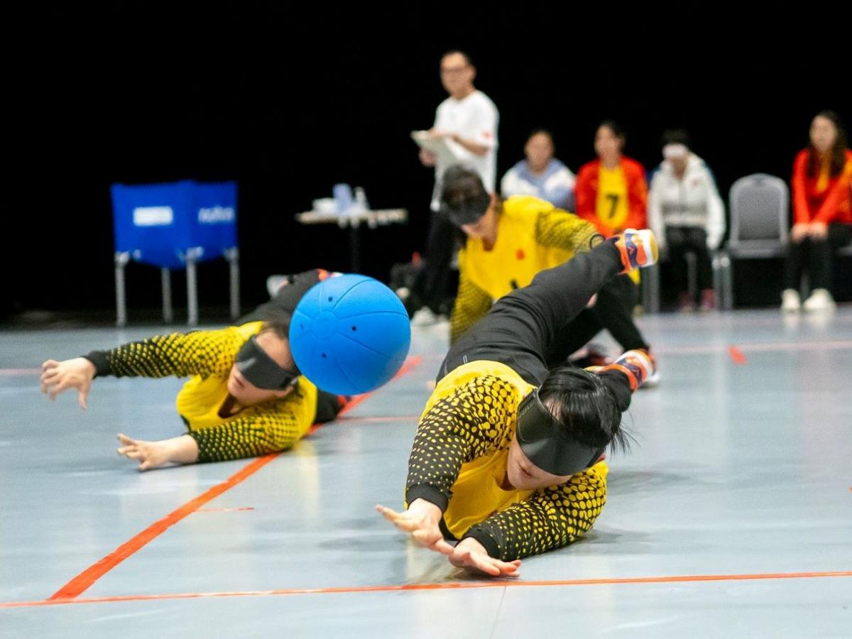 Two female athletes block a blue ball during a goalball match