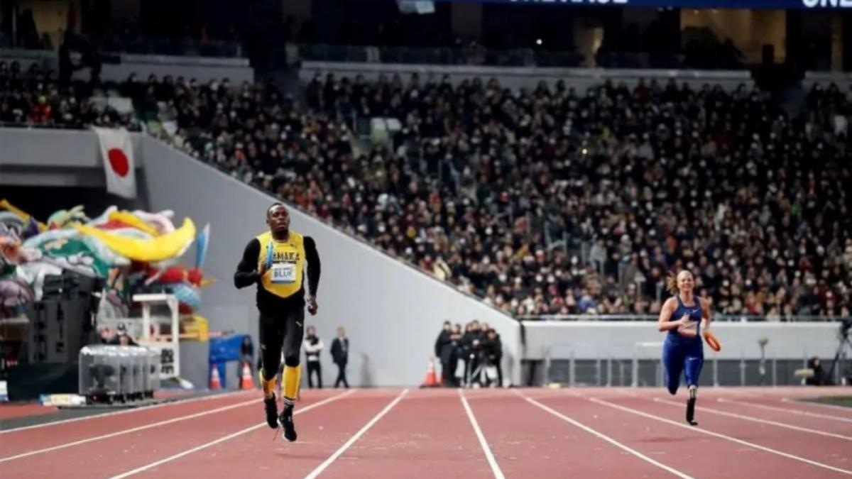 A male sprinter and a female sprinter run on the track of a packed stadium while holding relay batons.