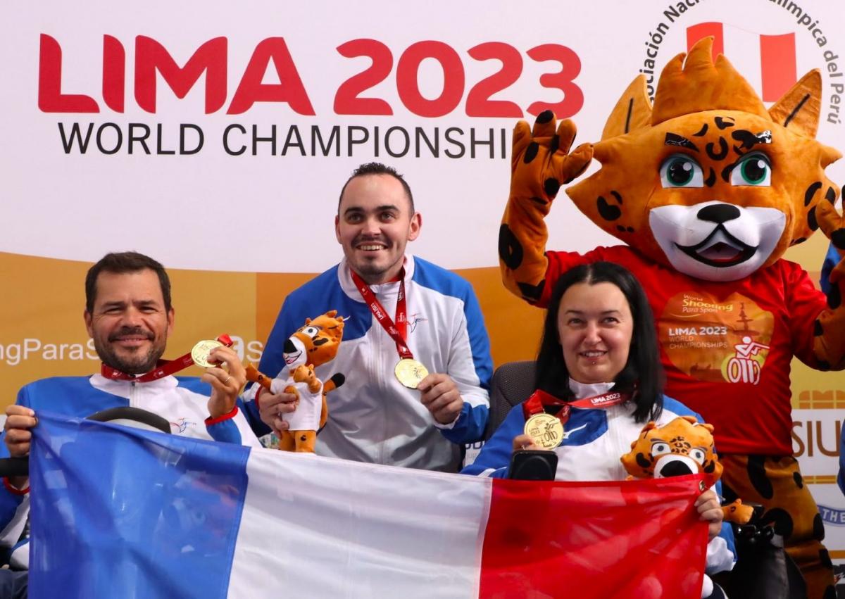 Two men and a woman holding the French flag near a mascot