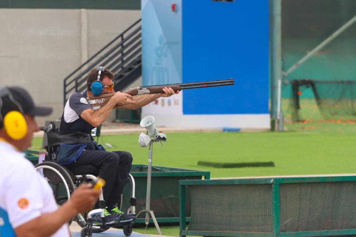 A man in a wheelchair in an outdoor Para trap shooting event