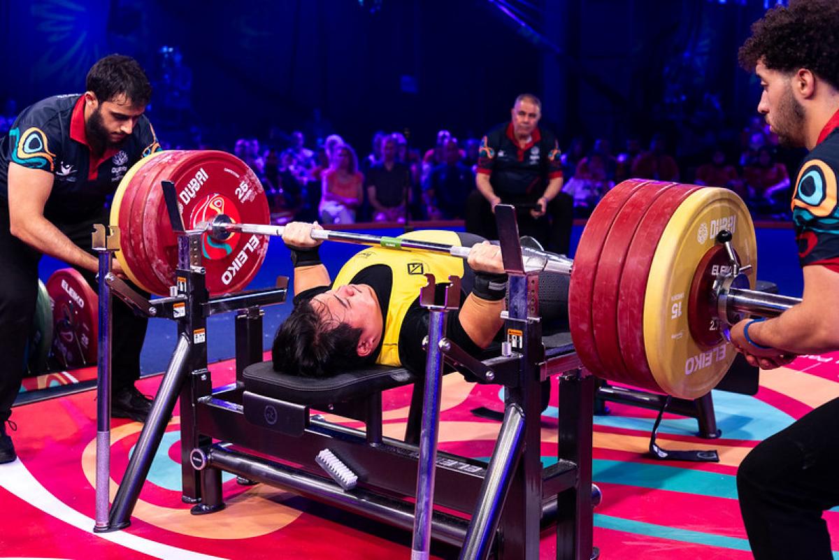 A short stature man lifting a bar in a Para powerlifting competition