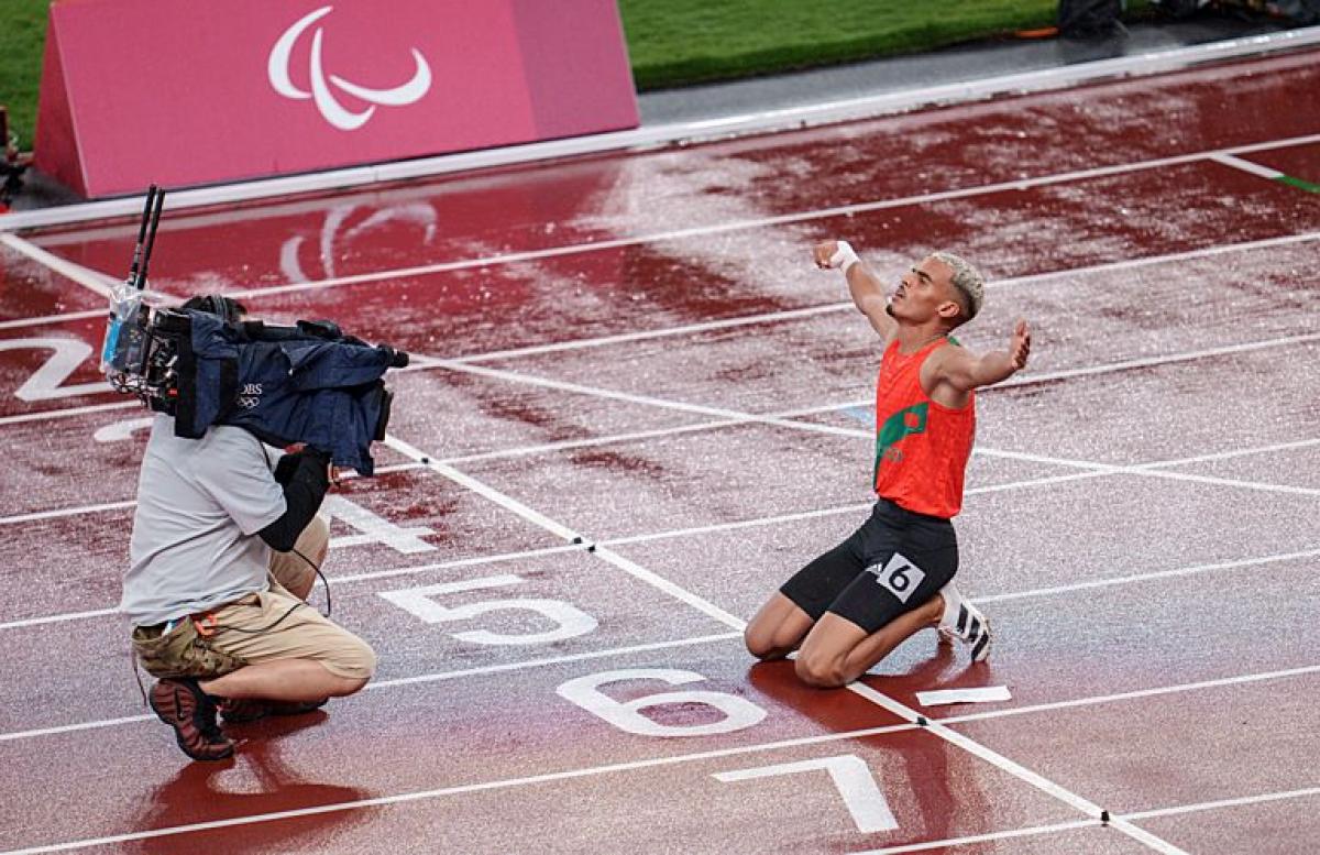 A male athlete celebrates in front of a camera operator on the track after winning a race.