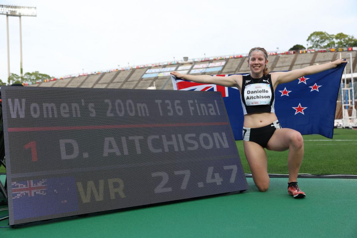 A young female athlete posing for a picture next to a screen showing a world record