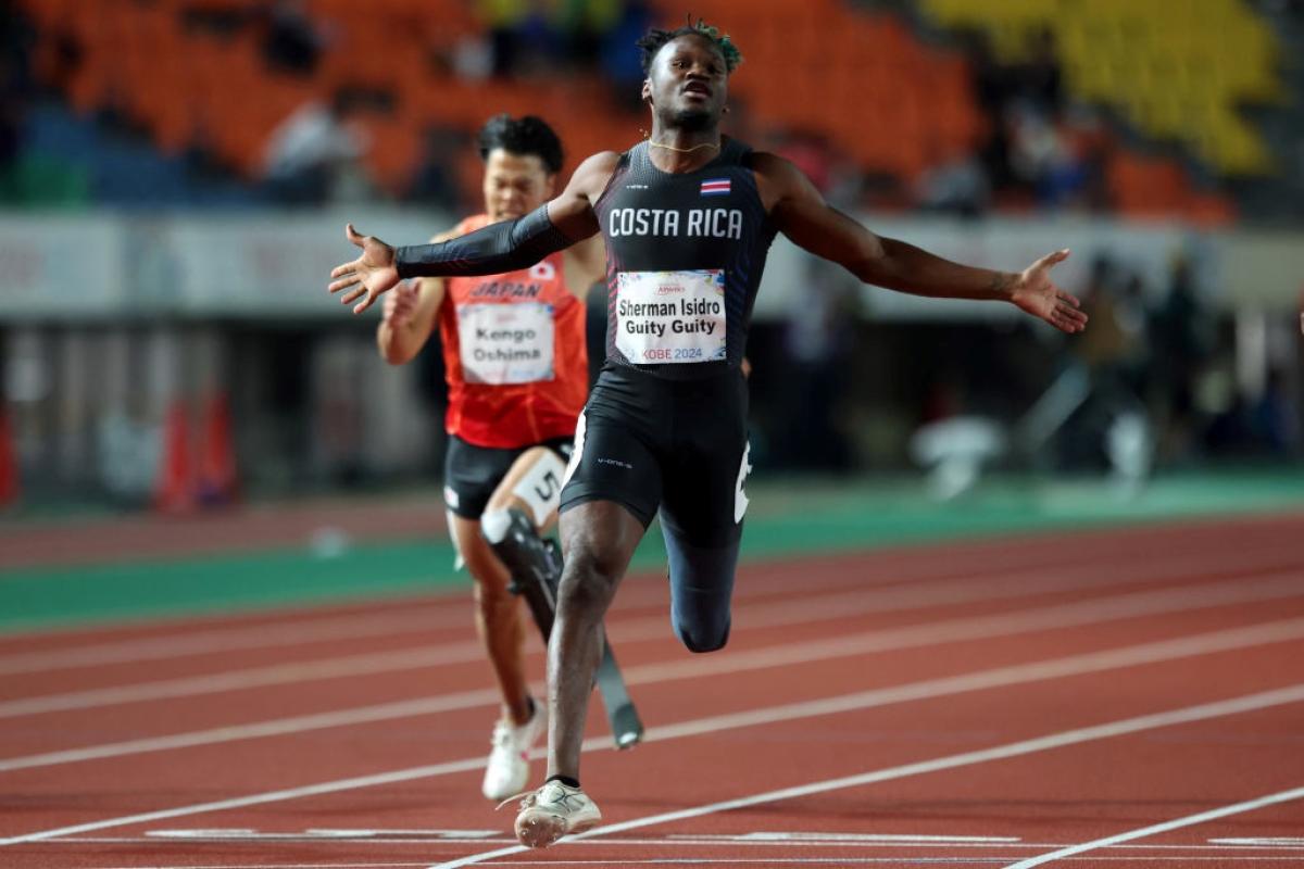 A male athlete with prosthetic leg crossing the finish line ahead of another competitor