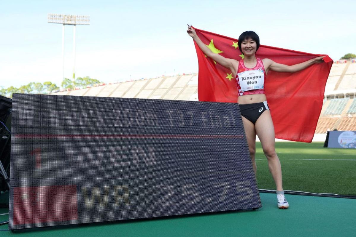 An athlete with the Chinese flag posing next to a scoreboard
