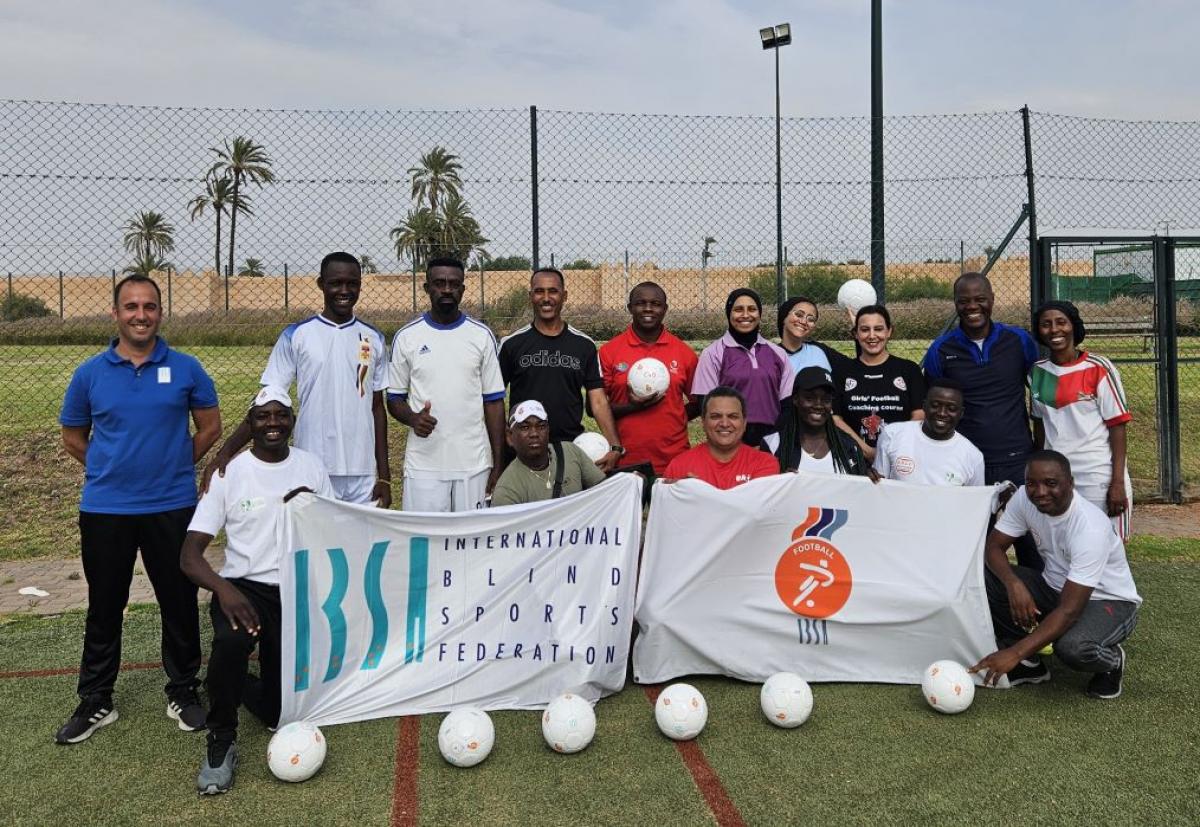 Sixteen people pose for a photograph with IBSA flags