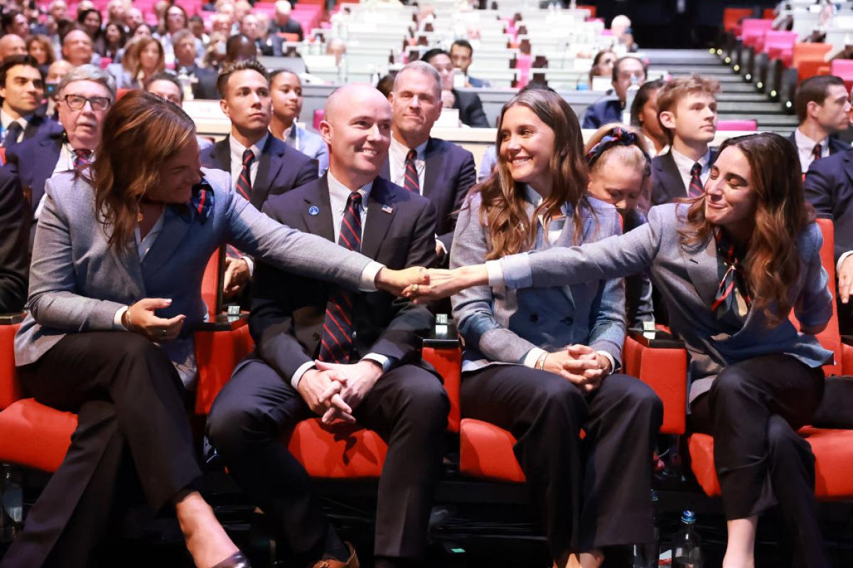 Four people sit side by side, with two of them holding each other's hands to celebrate