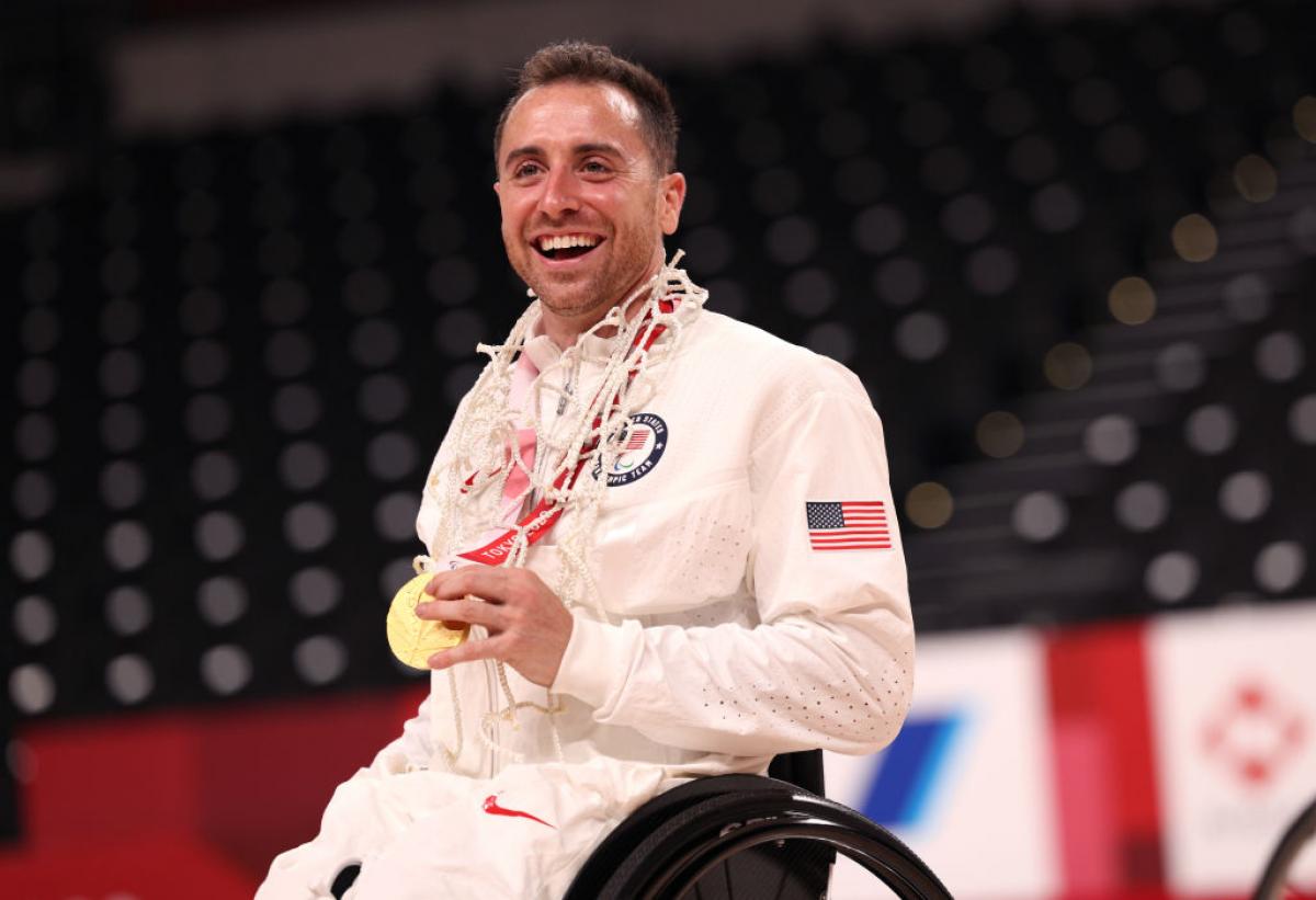 A male wheelchair basketball player posing for a photo while holding a gold medal. 