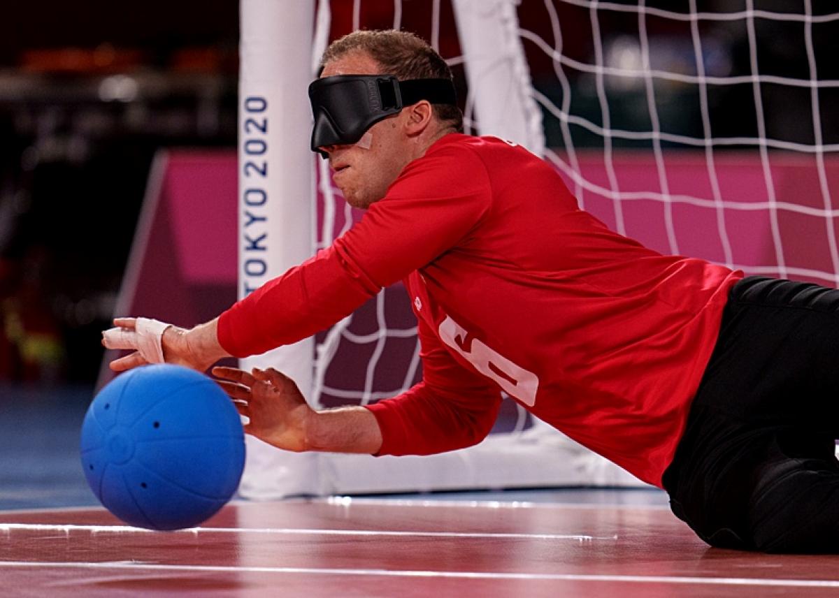 Two male goalball athletes are blocking the ball in front of a net