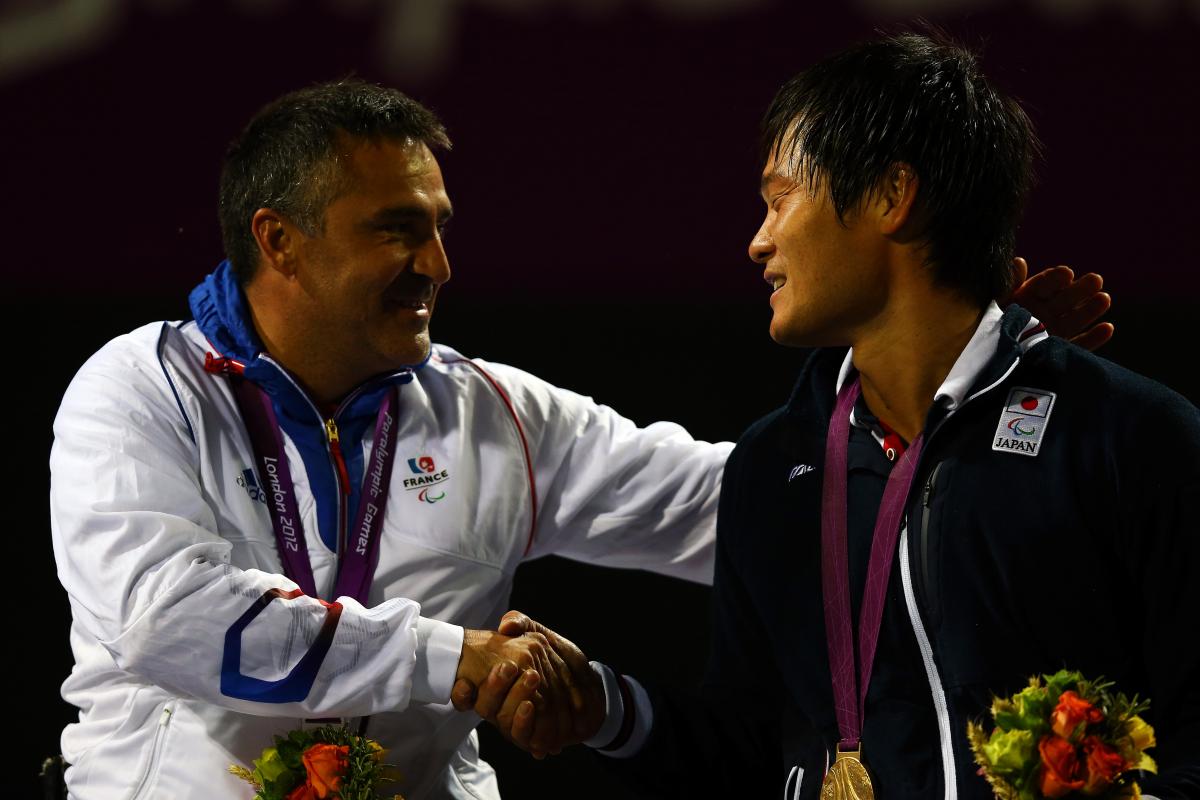 A picture of two men in a wheelchair shaking their hands