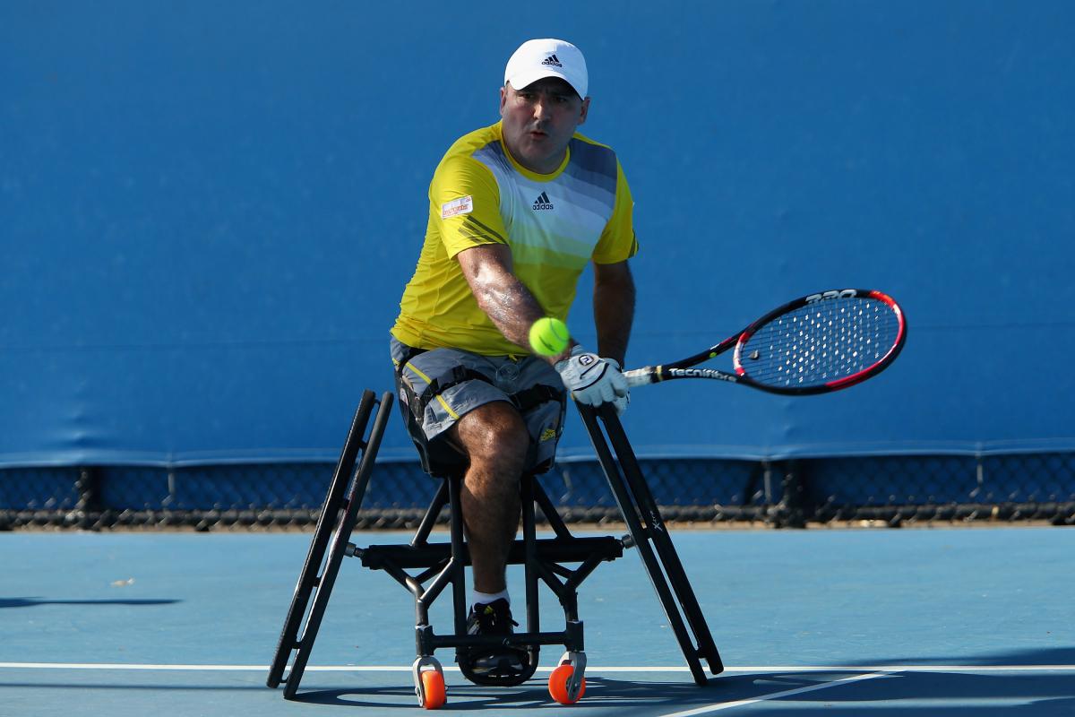 A picture of a man in a wheelchair playing a backhand during a wheelchair tennis match