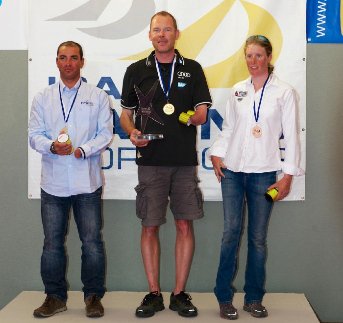 Three sailors are pictured receiving their medals on a podium. 