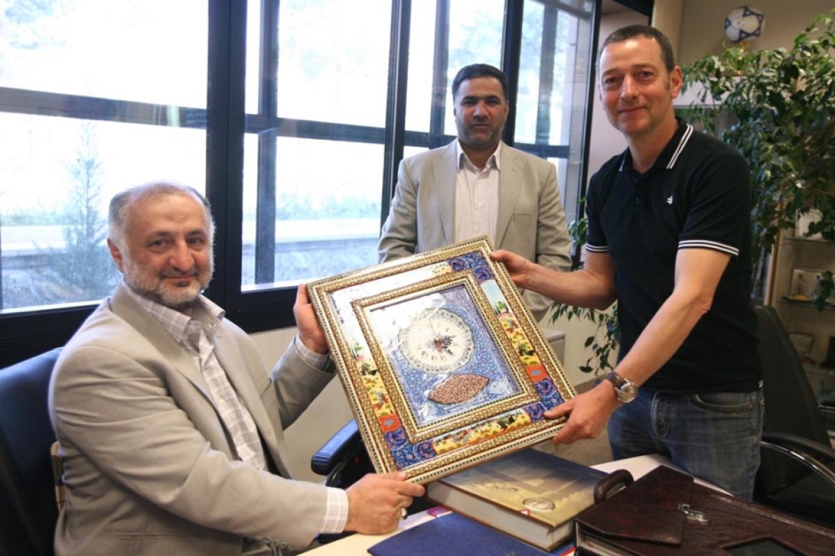 Two NPC Iran officials and reporter Ned Boulting hold up a framed award. 