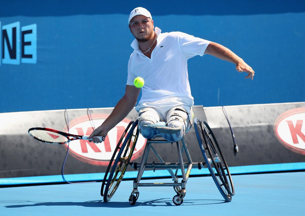 A wheelchair tennis player hits a forehand with his right hand. 