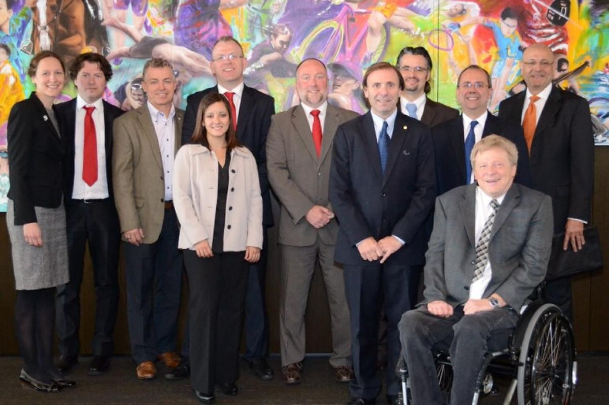 A group shot of 11 smartly dressed people lined up in front of a painted sport wall mosaic looking directly at the camera