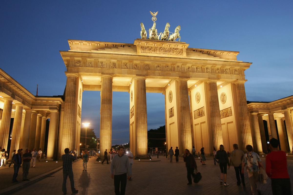 Illuminated gate in twilight. People passing by in front of the gate