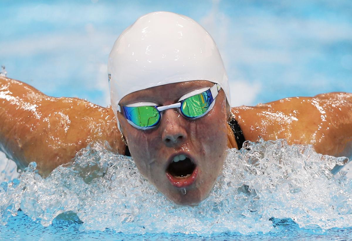 Women wearing swim goggles and a swim cap taking breath while swimming butterfly stroke.