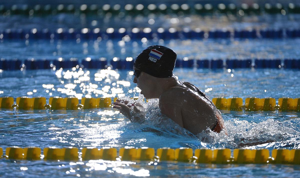 Women with black swim cap swimming breast stroke. Her head is out of the water as she is taking a breath