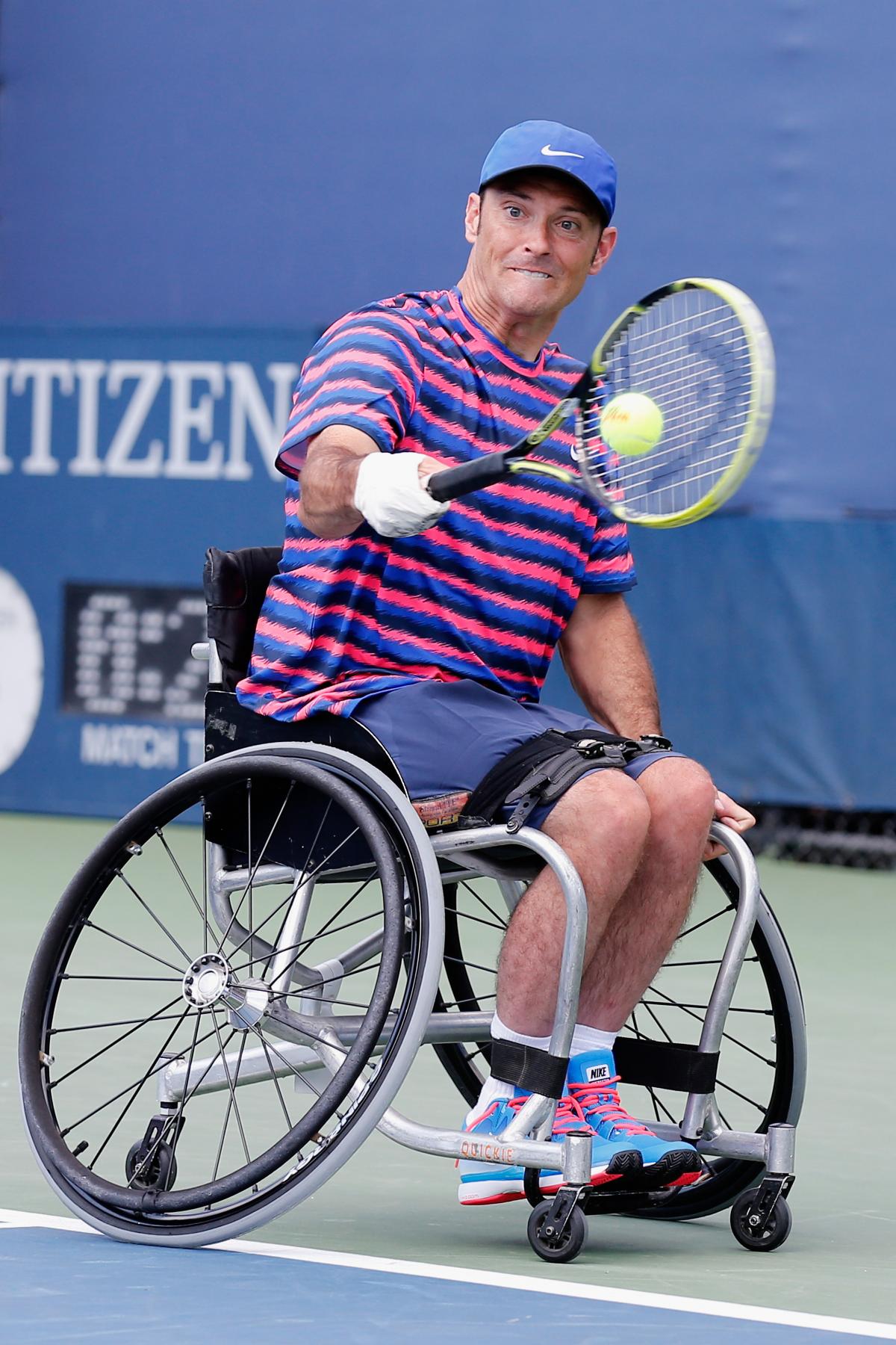 Man in wheelchair with tennis racket on the field.