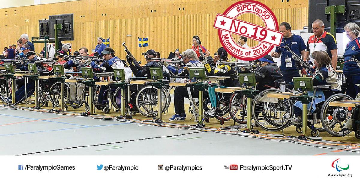 A line of seated athletes holding rifles line up for competition.