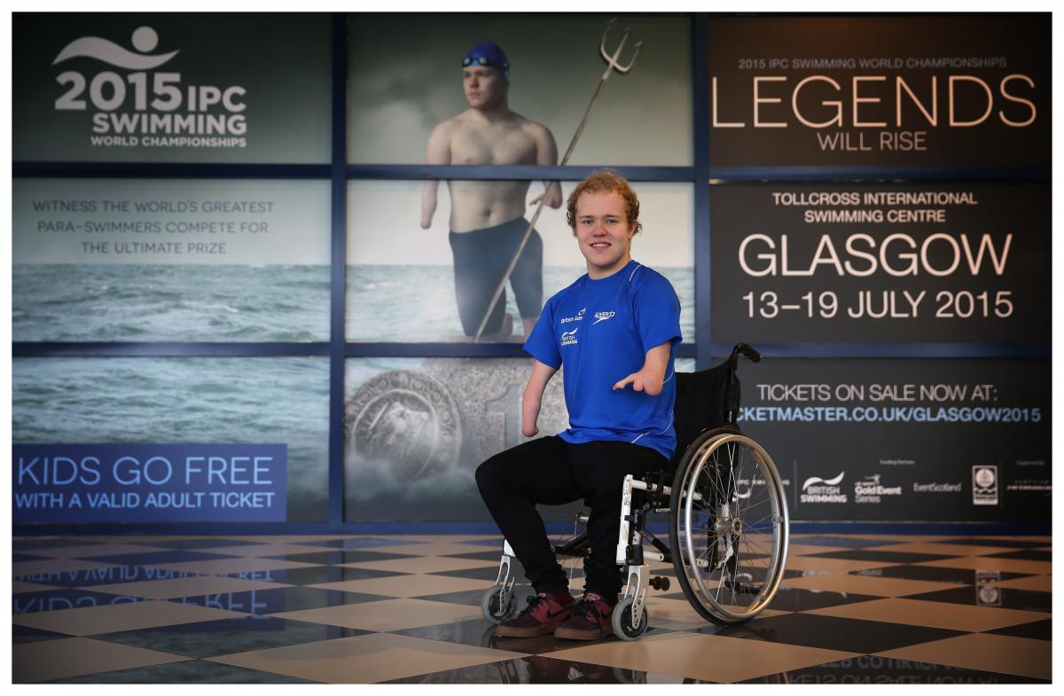 Man in wheelchair poses in front of a wallpaper