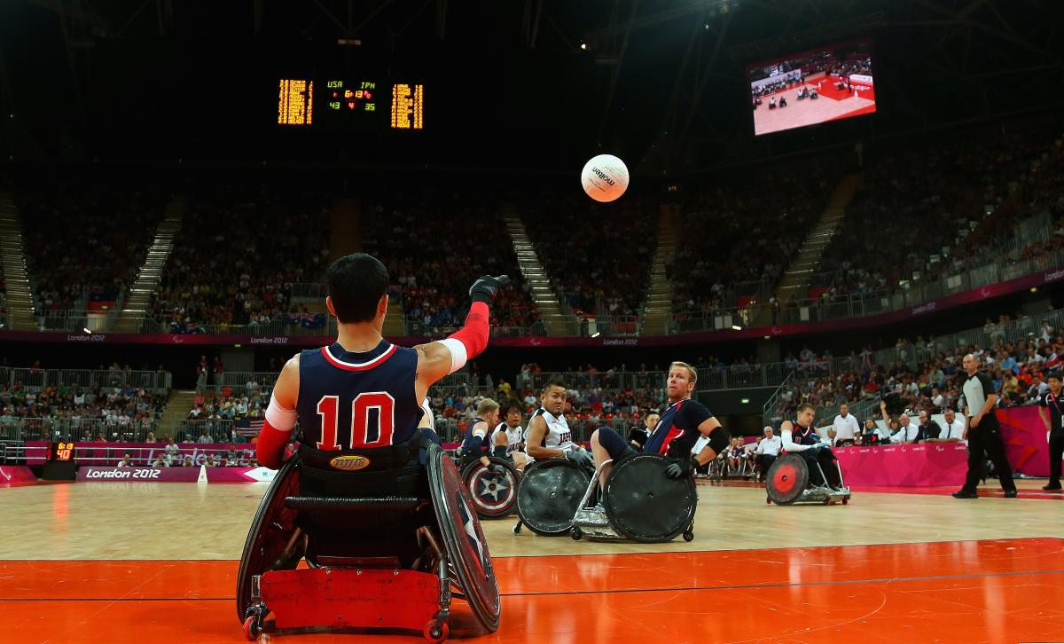 Man in wheelchair throwing a ball, two other men trying to catch it