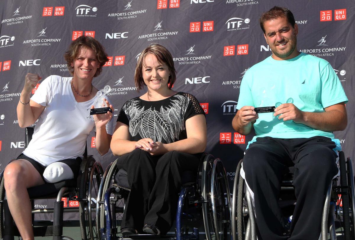 Three people in wheelchairs posing in front of a branded backdrop