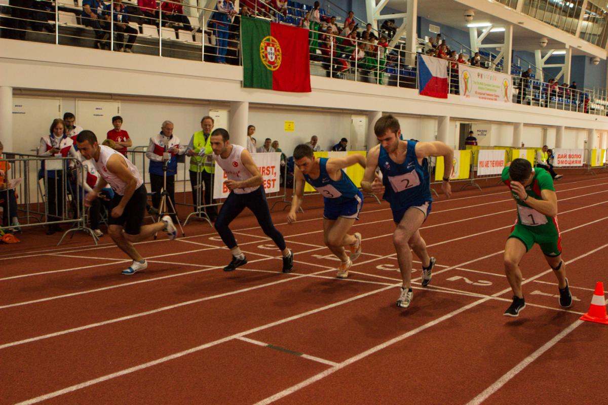 Five young men run on an athletics track next to each other