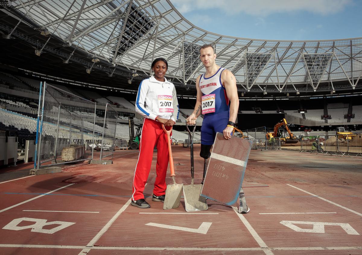 A man and a woman in a stadium, with spadens, working on an athletics track